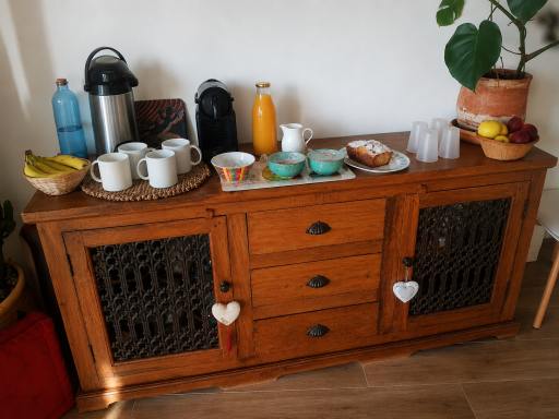 Buffet collation Buffet en bois avec tasses, assiettes, fruits et boissons disposés dessus.